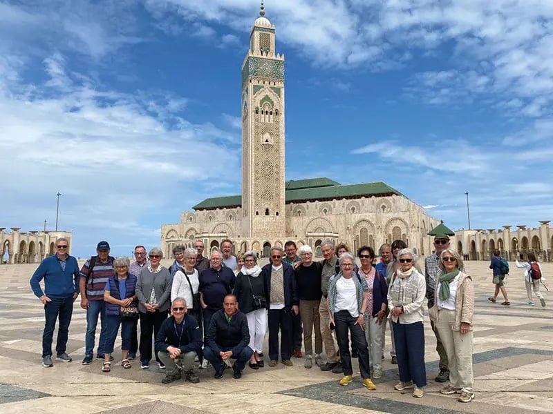 Gruppe von älteren Menschen vor großer Moschee mit hohem Minarett auf einem weiten Platz
