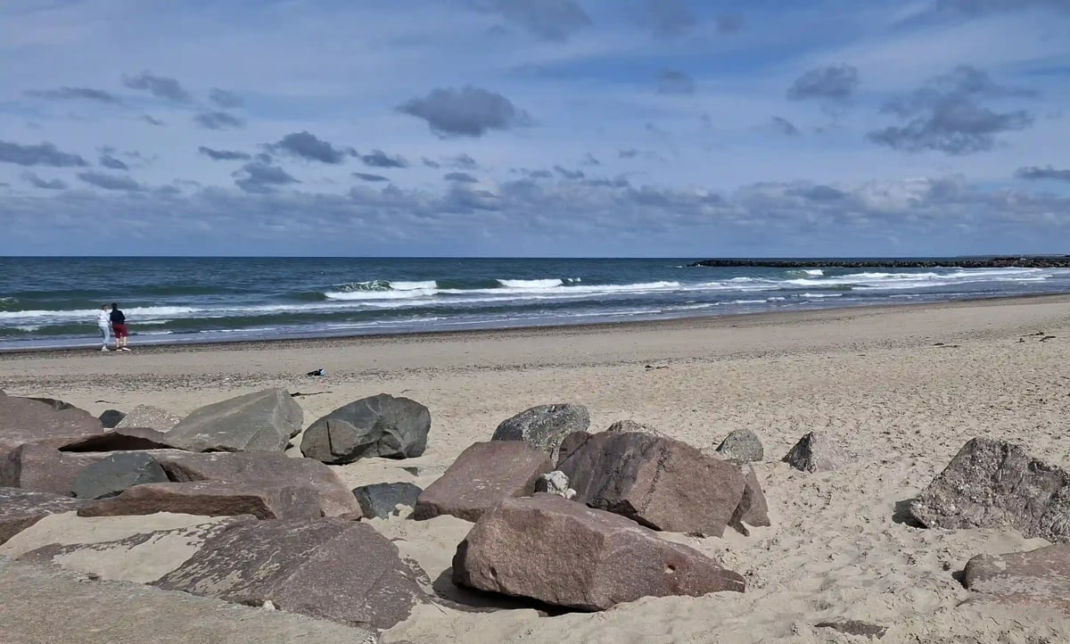 Weiter Sandstrand an der dänischen Küste mit Wellen und bewölktem Himmel