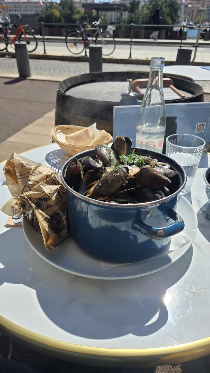 Topf mit Miesmuscheln und Brot auf einer sonnigen Restaurantterrasse