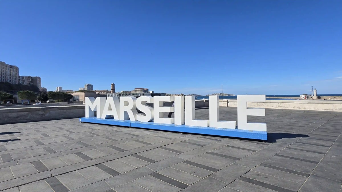 Grosse weisse Marseille-Buchstaben an der Hafenpromenade unter blauem Himmel