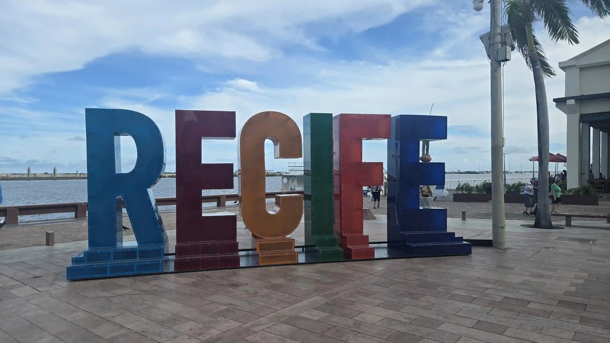 Bunte Recife-Buchstaben an einer Uferpromenade mit Palmen und Meer im Hintergrund