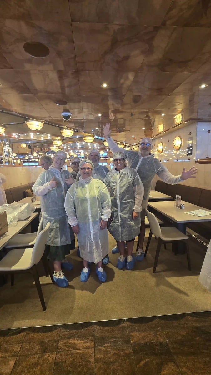 Reisegruppe in Schutzkleidung und Überschuhen an Bord eines Kreuzfahrtschiffs