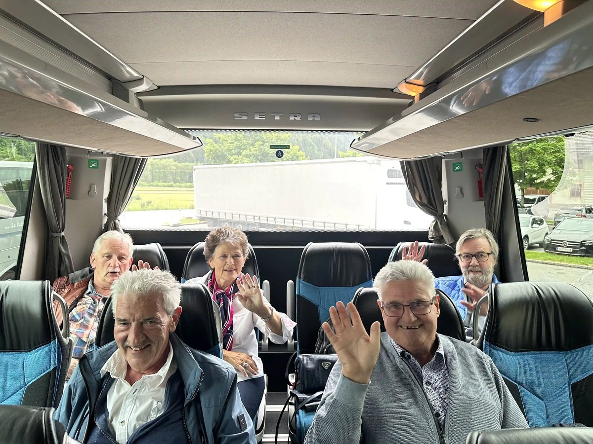 Reisegruppe sitzt gut gelaunt im Car und winkt in die Kamera.