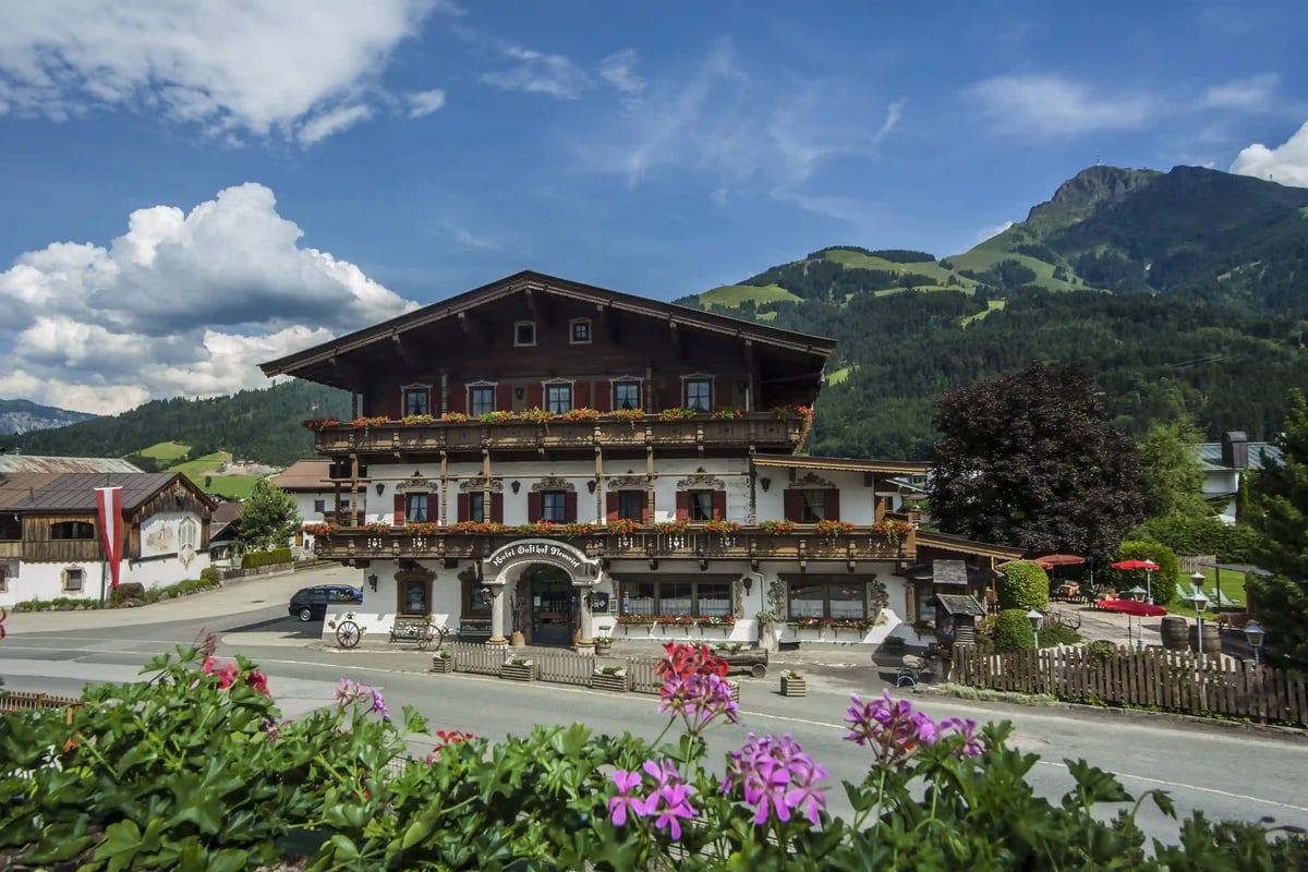 Traditionelles Berghotel vor einer eindrucksvollen Alpenkulisse bei sonnigem Wetter.