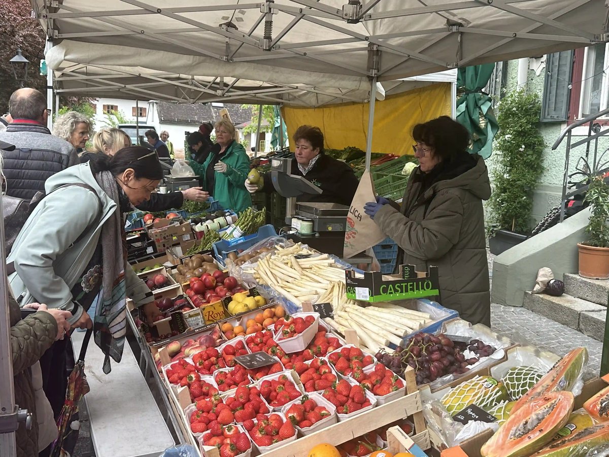 Marktstand mit frischem Obst, Gemüse und Spargel, an dem mehrere Personen einkaufen.