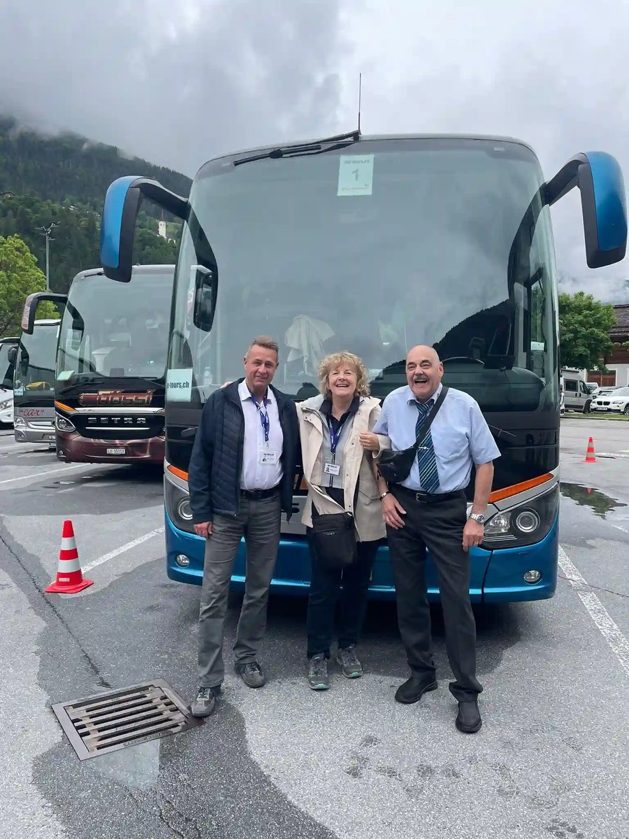 Drei Teilnehmende stehen lächelnd vor dem Reisecar und freuen sich auf den Ausflug.