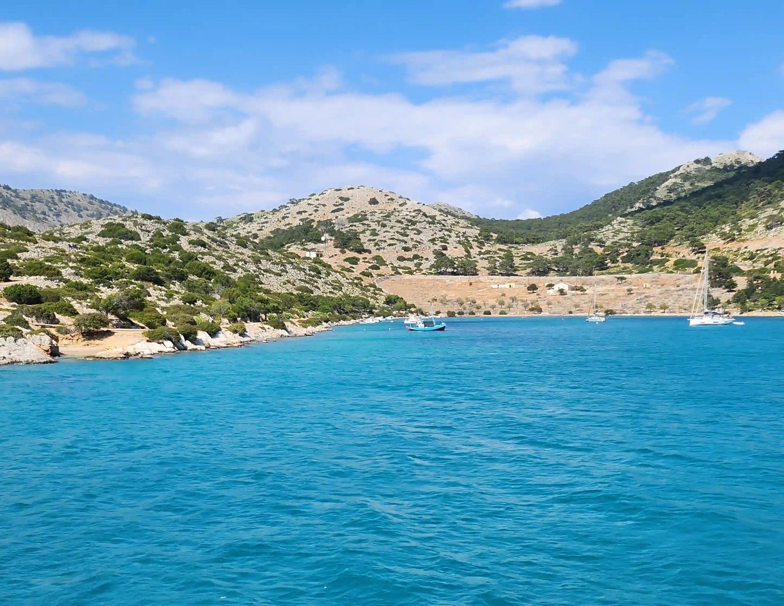 Türkisblaue Bucht mit felsiger Küstenlandschaft und Segelbooten bei Symi