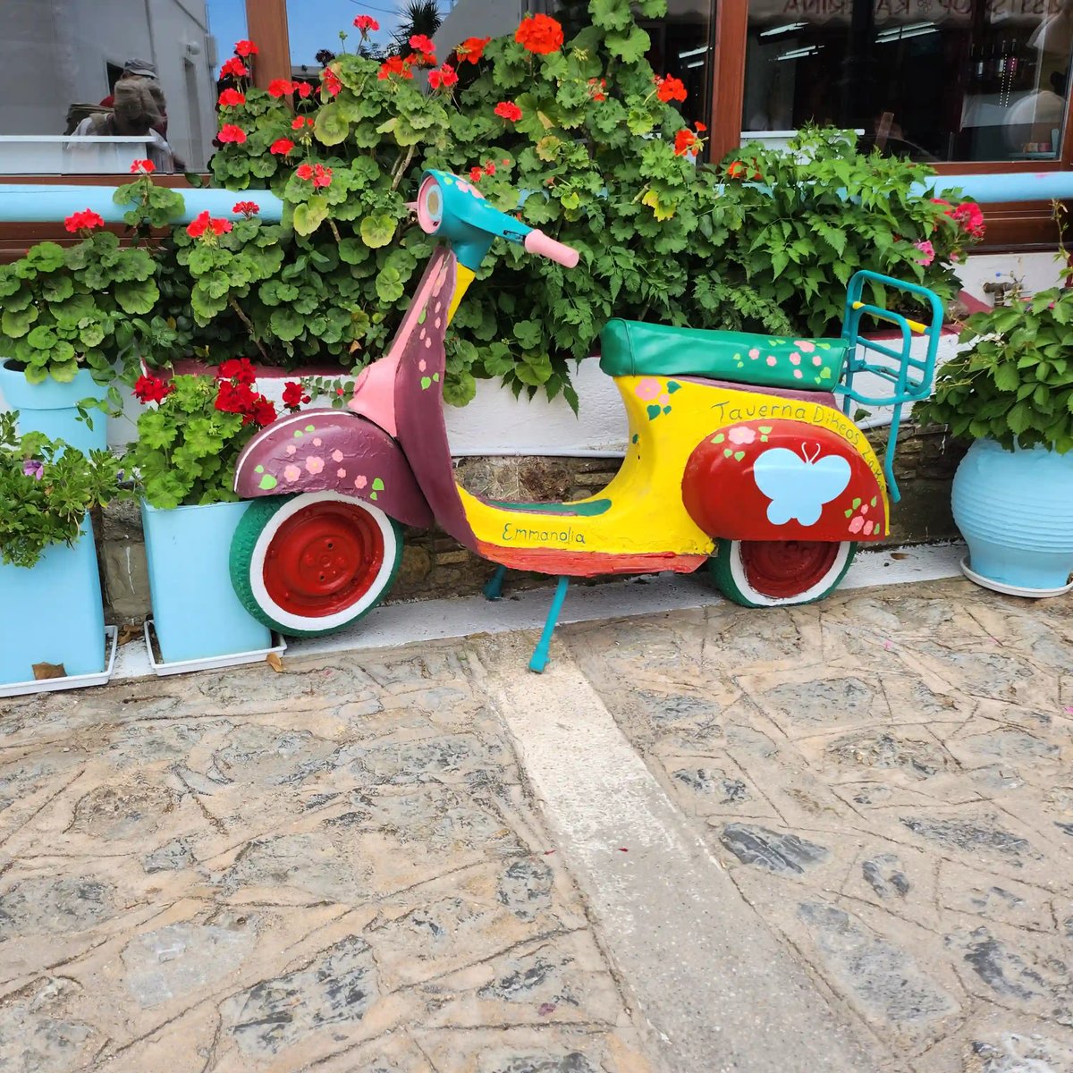 Farbenfroher Motorroller als Dekoration zwischen roten Blumen und Pflanzen