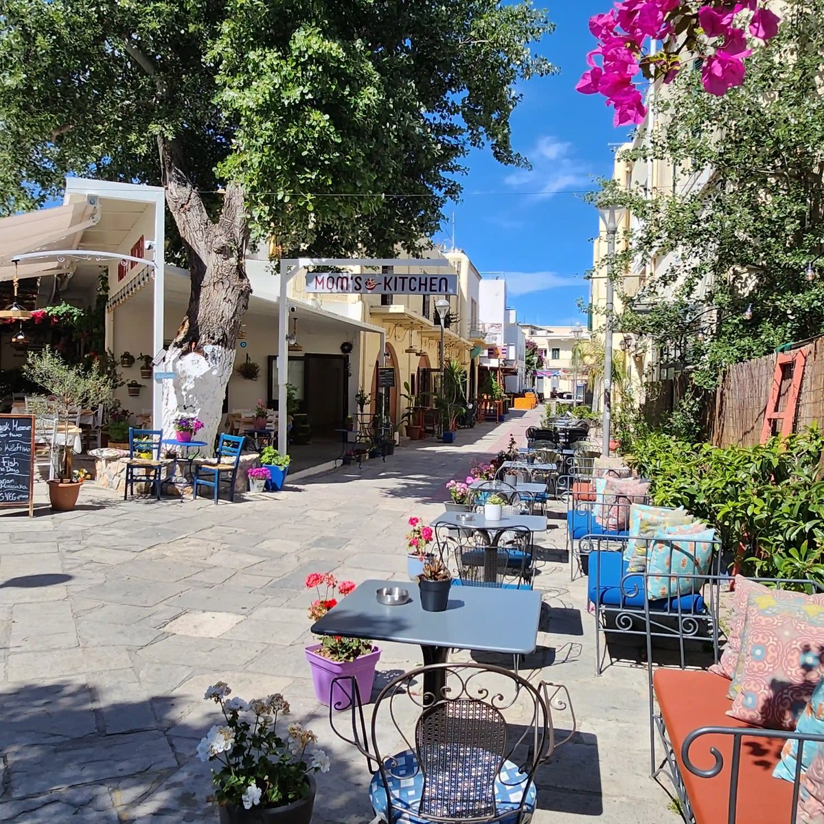 Sonnige Gasse in Kos-Stadt mit weissen Häusern, Restaurants und Sitzplätzen