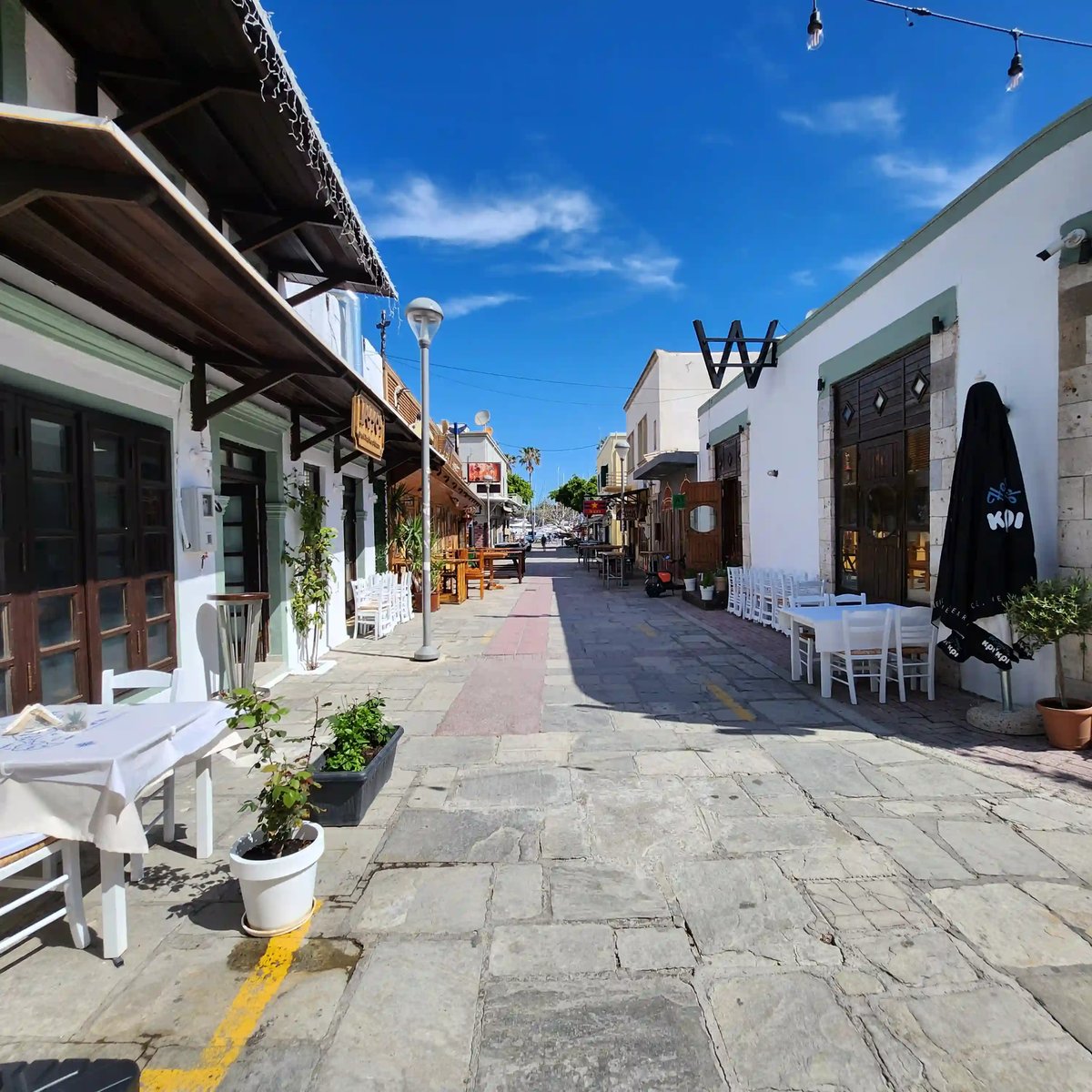 Sonnige Gasse in Kos-Stadt mit Restaurants, Sitzplätzen und blühenden Pflanzen
