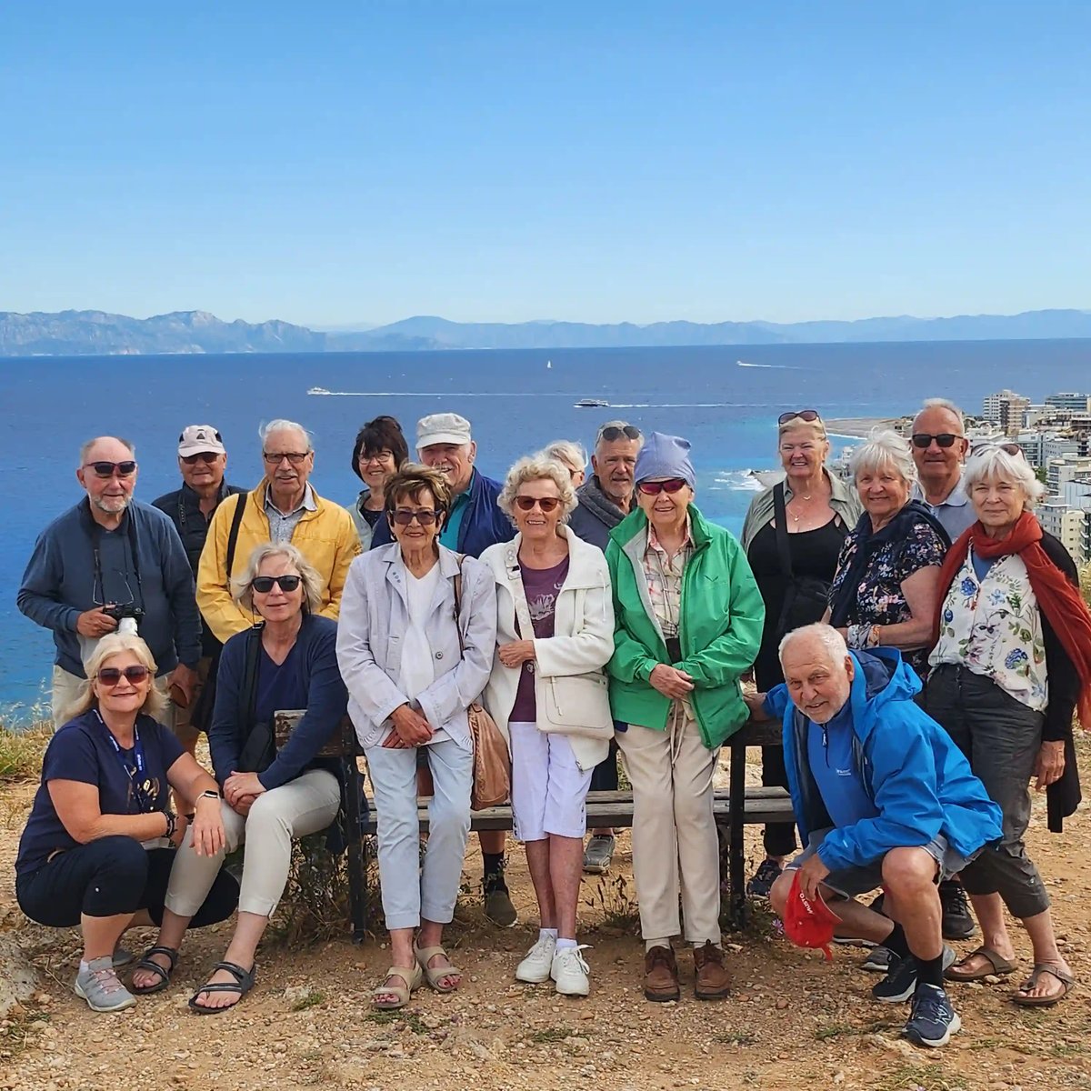 roupe de voyageurs devant un moulin à vent traditionnel entouré de palmiers à Kos. Reisegruppe vor Meer DE: Reisegruppe vor dem blauen Meer mit Blick auf die Küste von Rhodos
