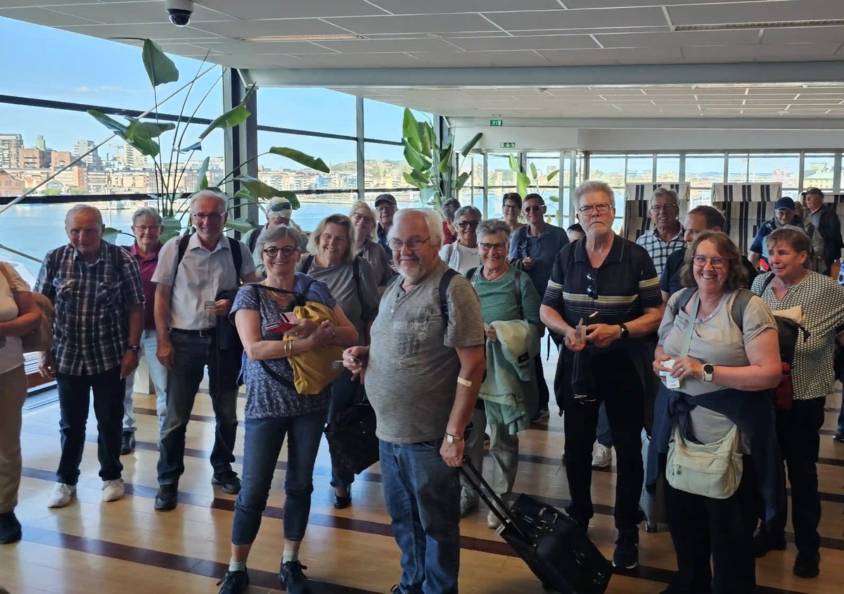 Gut gelaunte Reisegruppe mit Gepäck in einem hellen Fährterminal mit Blick aufs Wasser