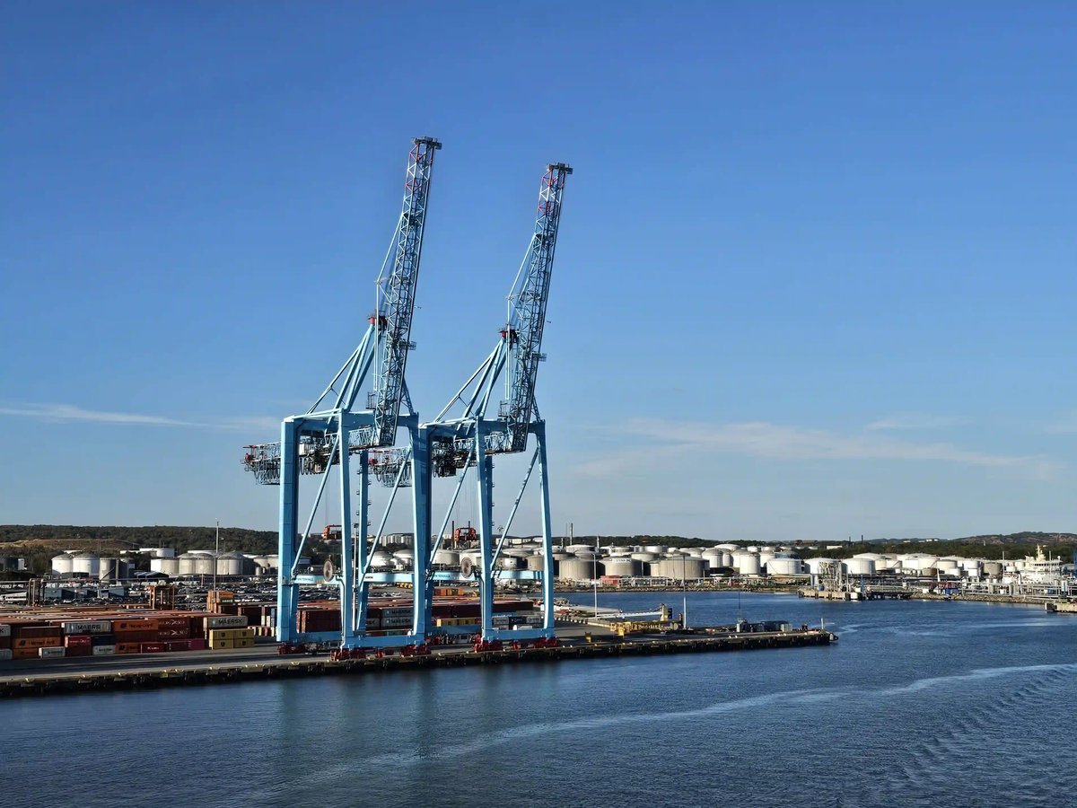 Grosse Containerkräne und Industrieanlagen an einem Hafenbecken unter blauem Himmel