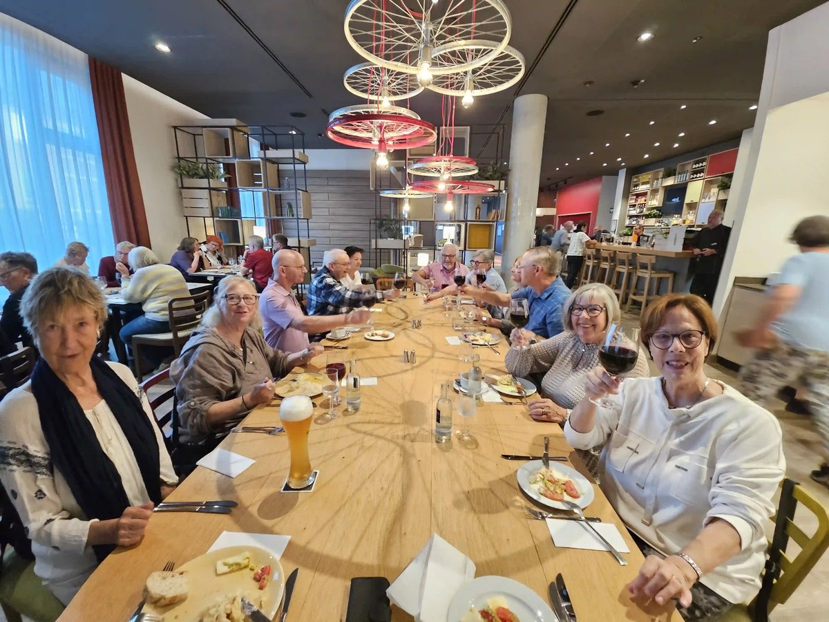 Reisegruppe sitzt gemeinsam an einem langen Tisch im Restaurant und stösst mit Getränken an