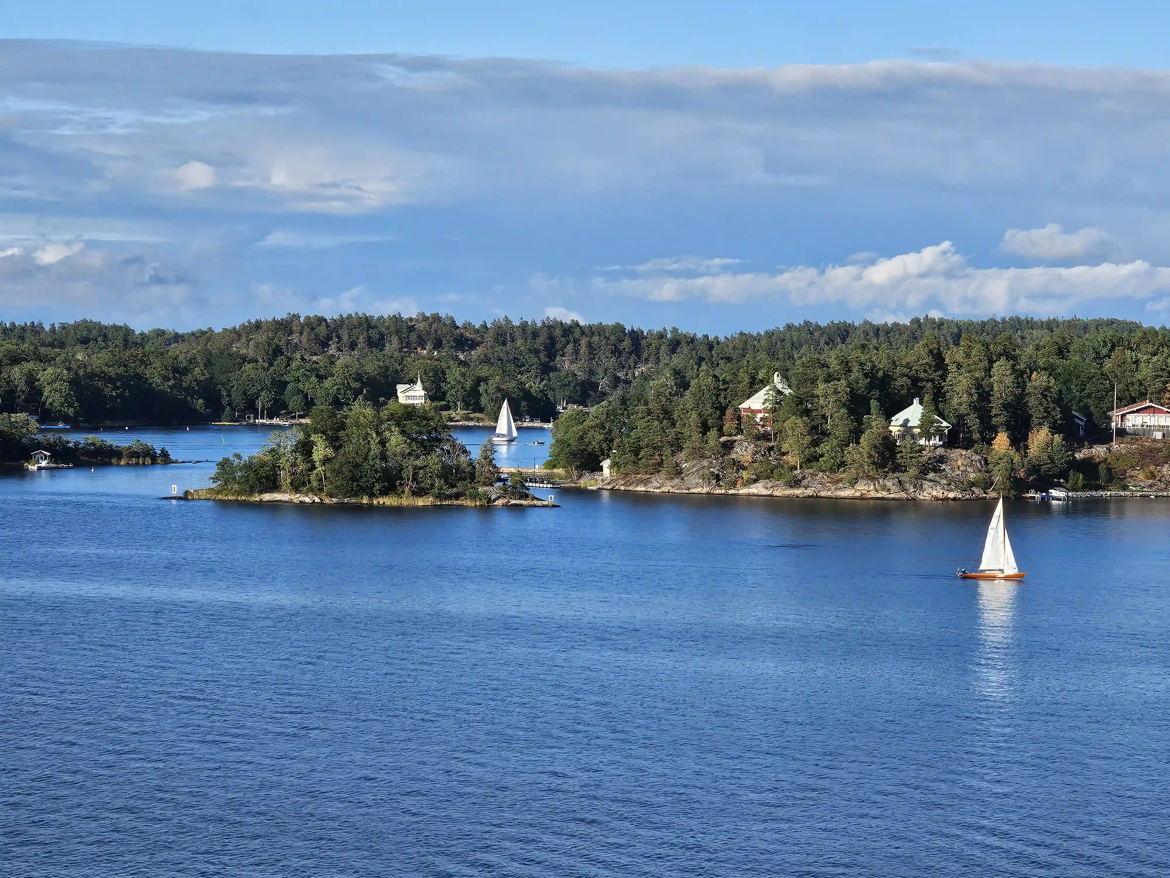 Bewaldete Schäreninseln mit Häusern und Segelbooten auf blauem Wasser in Schweden