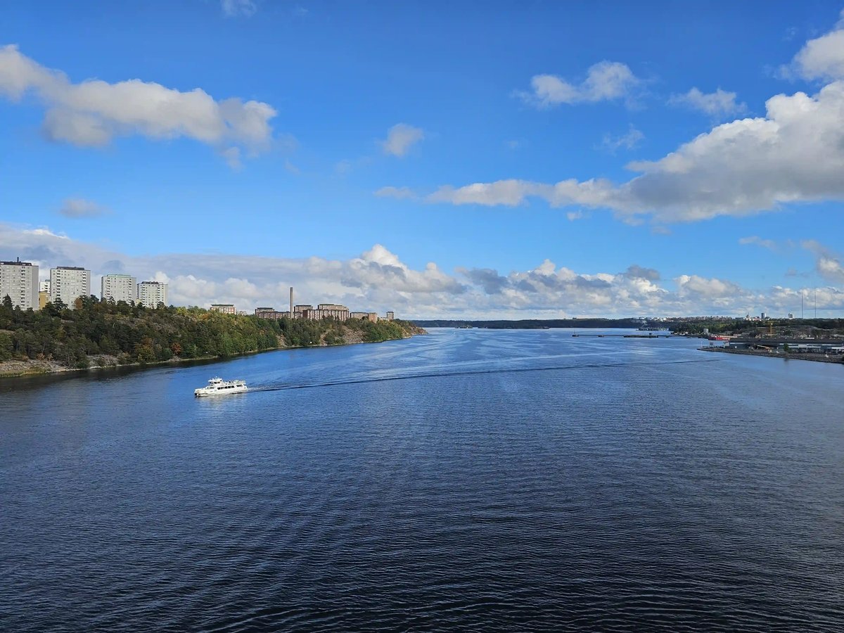 Breite Wasserstrasse bei Stockholm mit bewaldeten Ufern, Wohnhäusern und einem weissen Ausflugsschiff