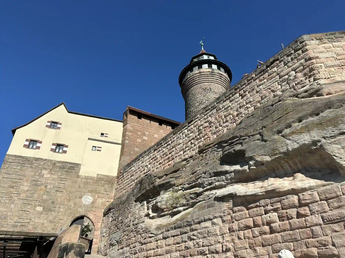 Blick auf die mächtigen Mauern und einen Turm der Kaiserburg Nürnberg unter blauem Himmel.