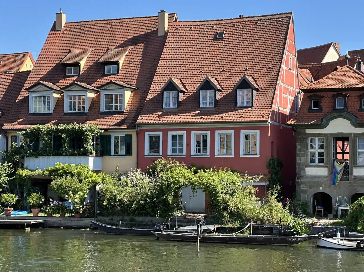 Historische Häuser mit roten Ziegeldächern und kleinen Booten direkt am Flussufer in Bamberg.