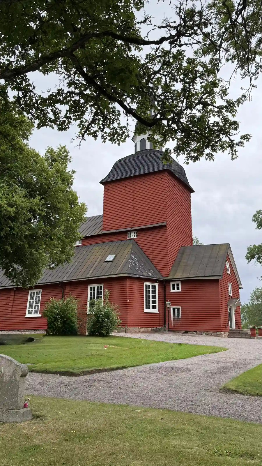 Rote Holzkirche von Habo, umgeben von Bäumen und einer gepflegten Grünanlage