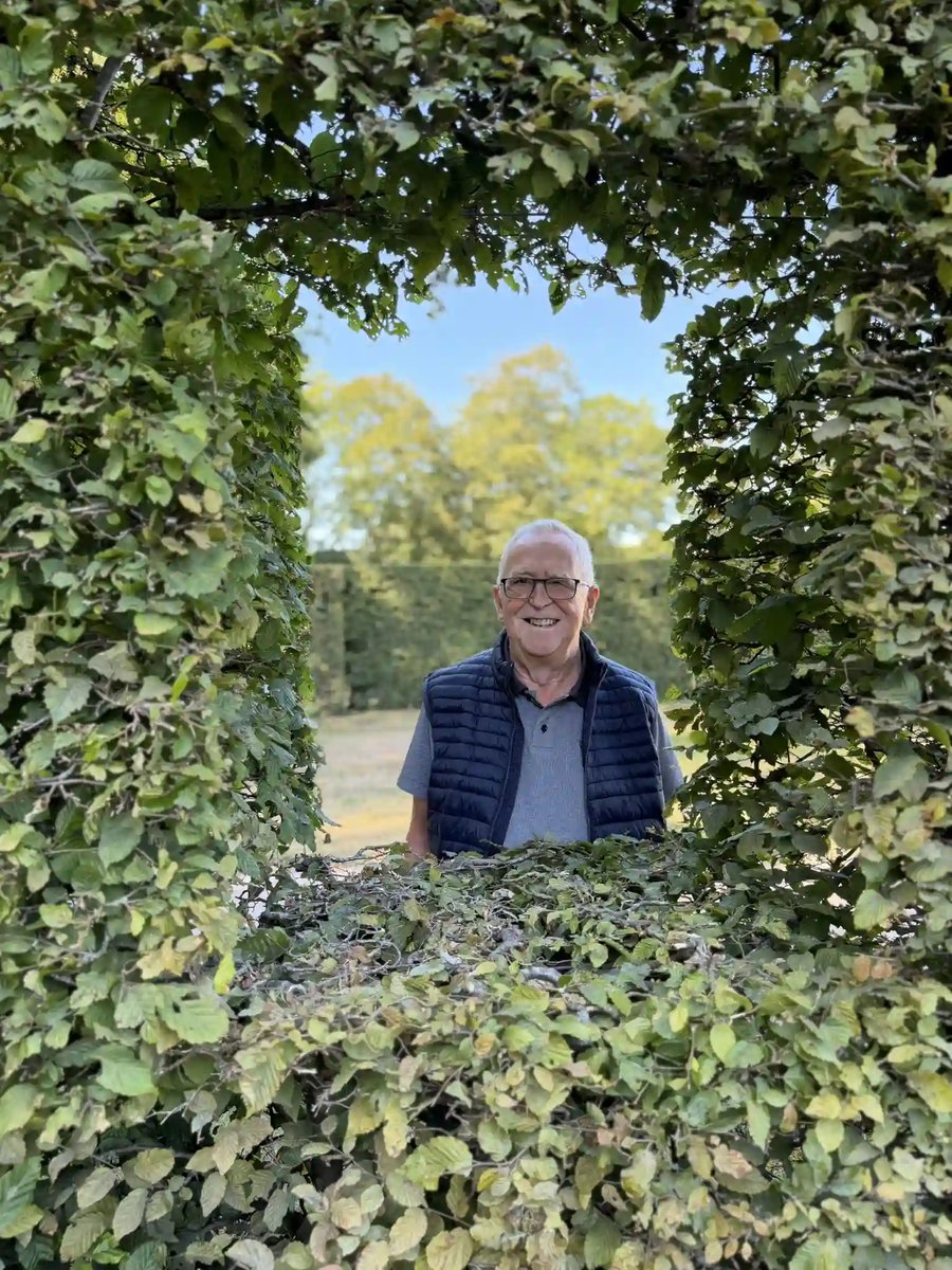 Lächelnder Reiseteilnehmer in einer kunstvoll geschnittenen grünen Hecke