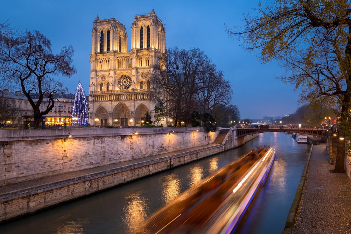 Beleuchtete Kathedrale Notre-Dame am Abend mit vorbeifahrendem Boot auf der Seine