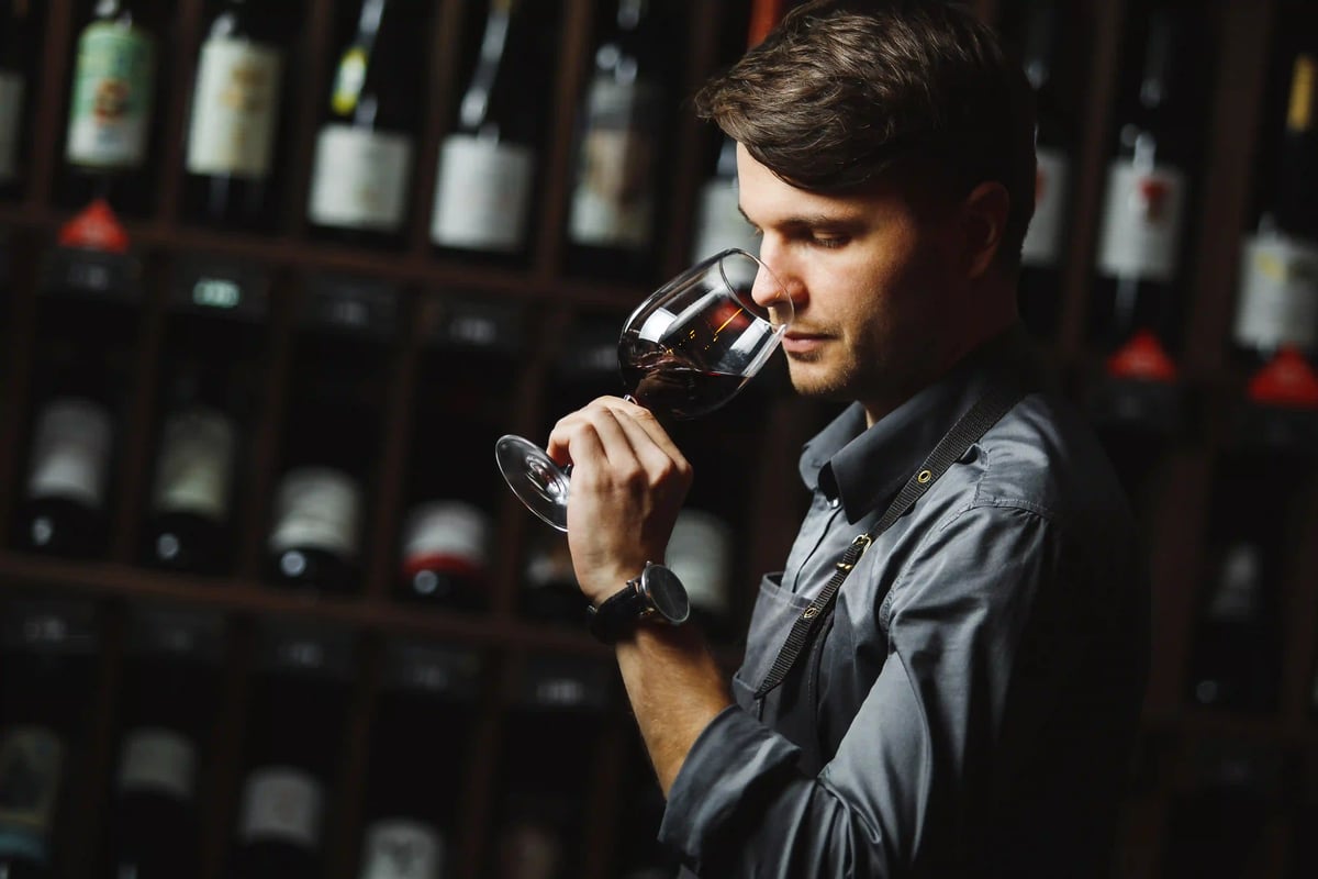 Mann verkostet Rotwein in einem Weinkeller vor gefüllten Regalen