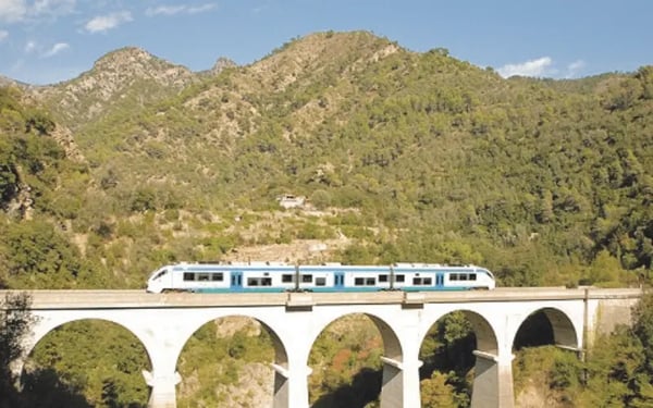 Zug fährt über steinernen Viadukt durch bewaldete Berglandschaft