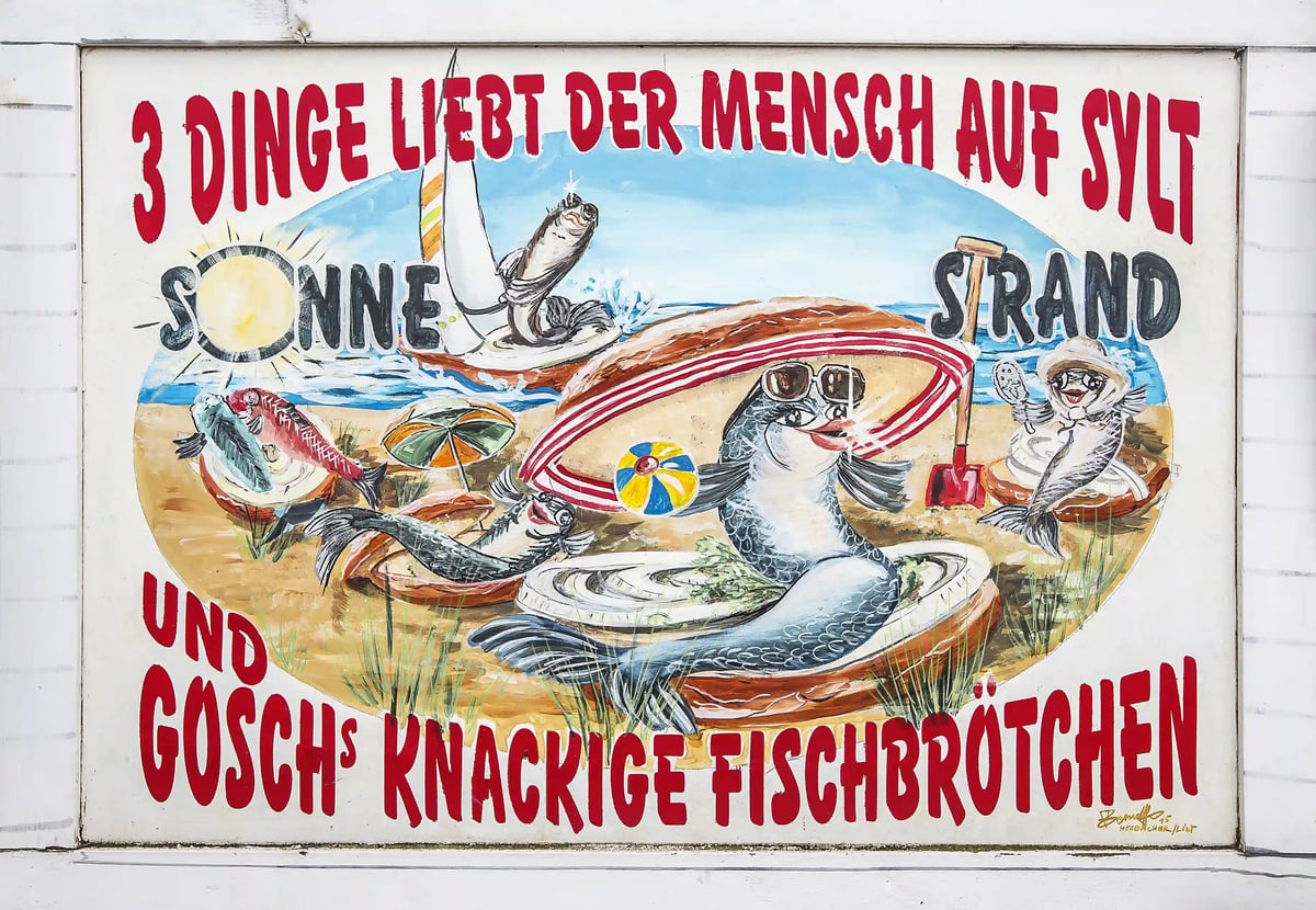 Bemaltes Schild mit humorvollen Fischmotiven rund um Sonne, Strand und Fischbrötchen.