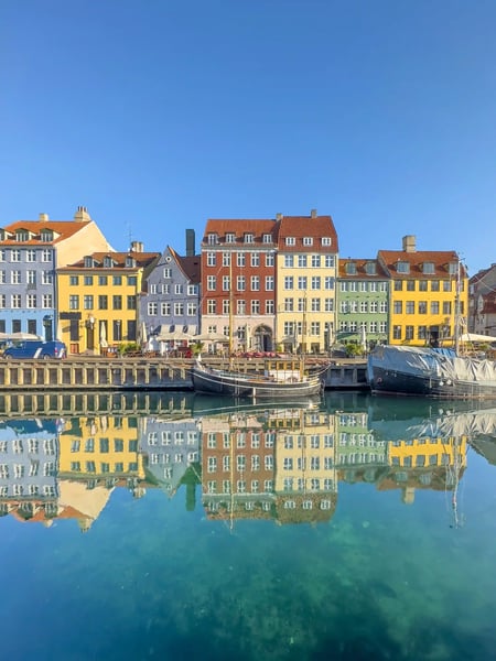 Bunte historische Häuser spiegeln sich im ruhigen Hafenbecken von Nyhavn in Kopenhagen bei klarem Himmel