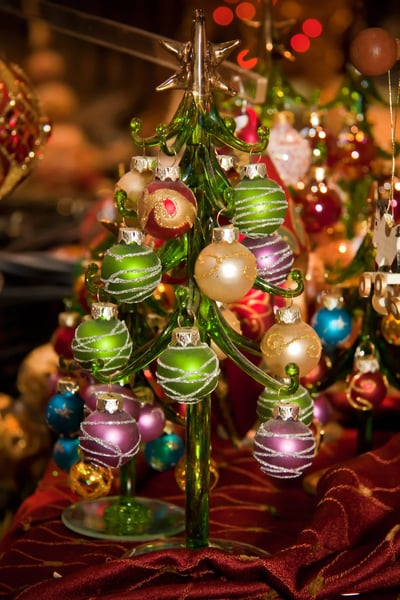 Kleiner dekorativer Weihnachtsbaum aus Glas mit bunten Christbaumkugeln auf einem festlich geschmückten Marktstand.