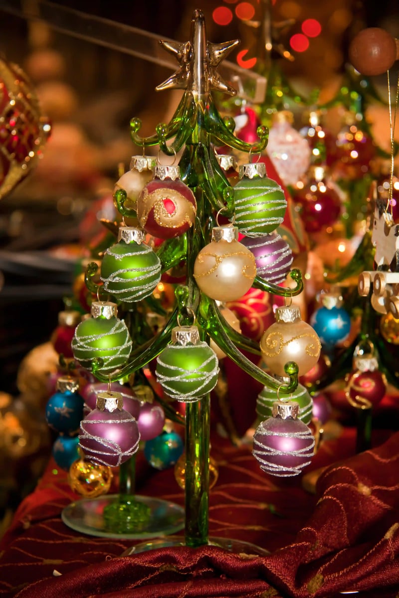 Kleiner dekorativer Weihnachtsbaum aus Glas mit bunten Christbaumkugeln auf einem festlich geschmückten Marktstand.