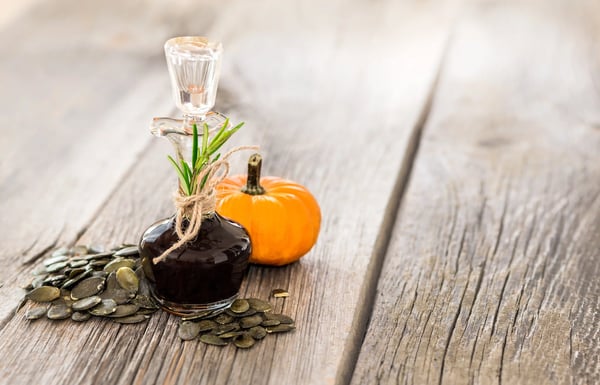 Flasche mit steirischem Kürbiskernöl neben Kürbis und Kürbiskernen auf Holzuntergrund