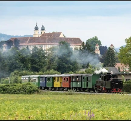 Historischer Stainzer Flascherlzug fährt durch grüne Landschaft mit Schloss im Hintergrund