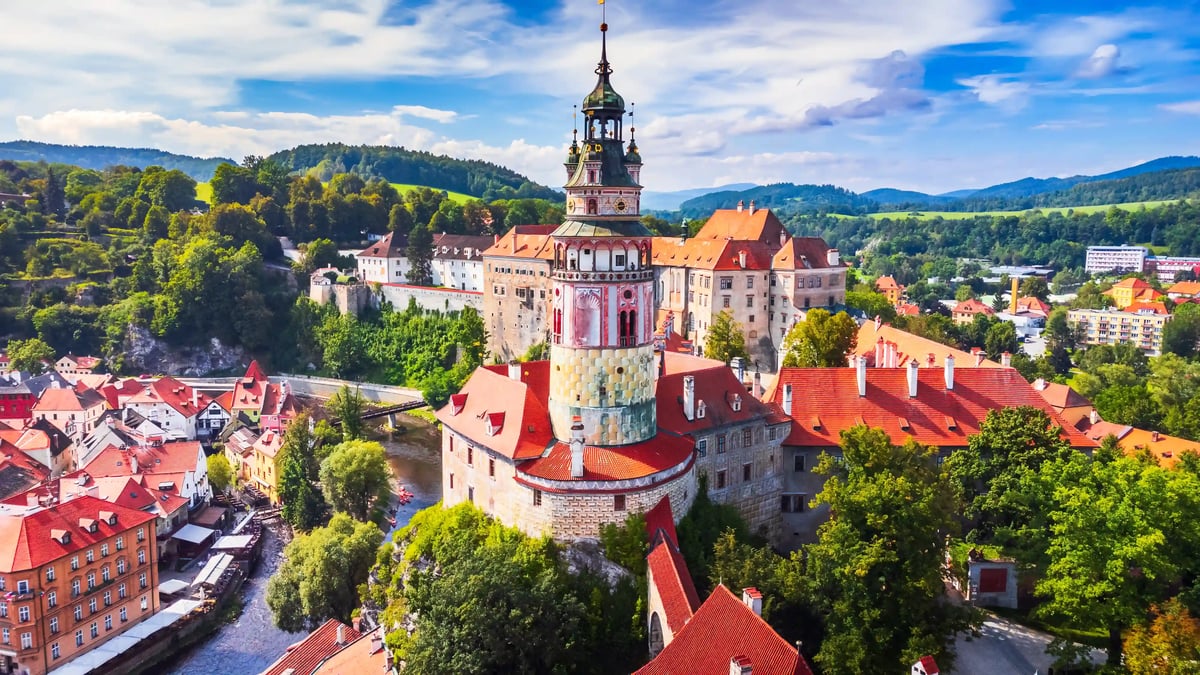 Blick von oben auf Schlossanlage mit rundem Turm und roten Dächern, Fluss und Altstadt ringsum