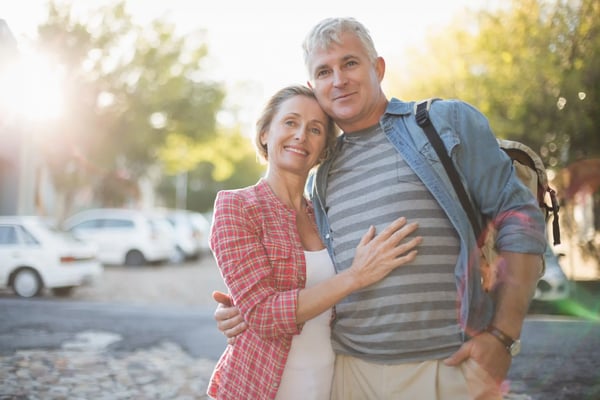 Glueckliches Paar umarmt sich draussen auf einem sonnigen Weg mit grünen Bäumen im Hintergrund