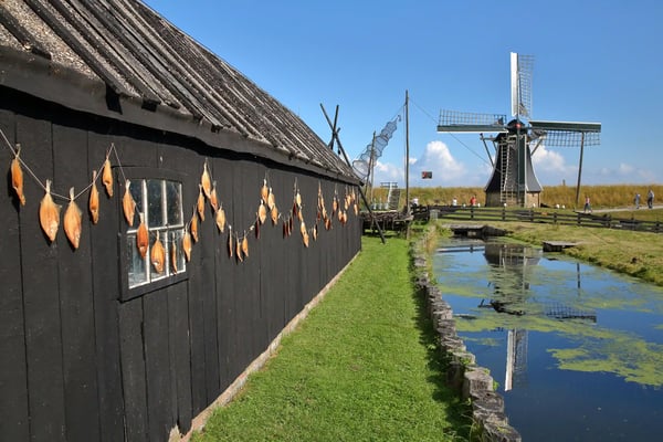 Traditionelle Windmühle neben Holzhaus in weiter flacher Landschaft mit Wasserlauf