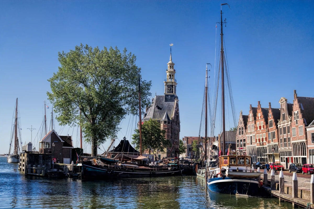 Historischer Hafen mit Segelbooten, ruhigem Wasser und traditionellen Häusern unter blauem Himmel