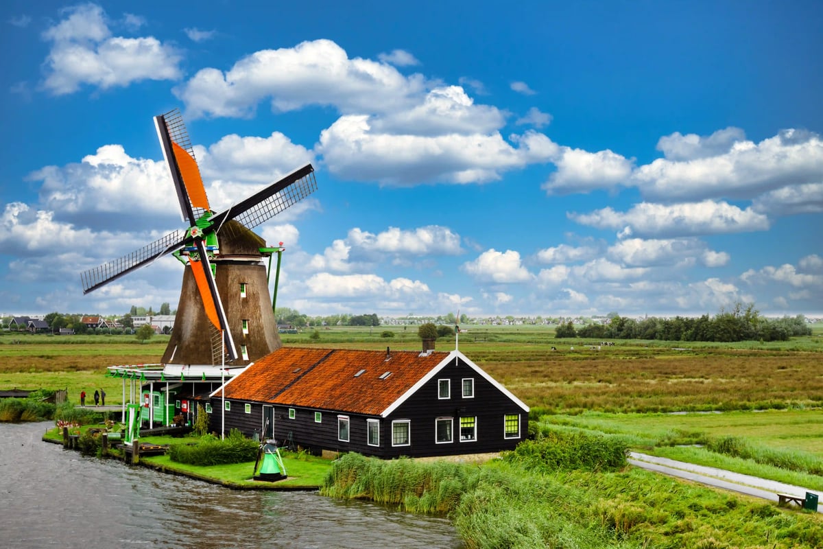 Schwarzes Holzhaus mit hängenden Fischen neben Wassergraben und Windmühle