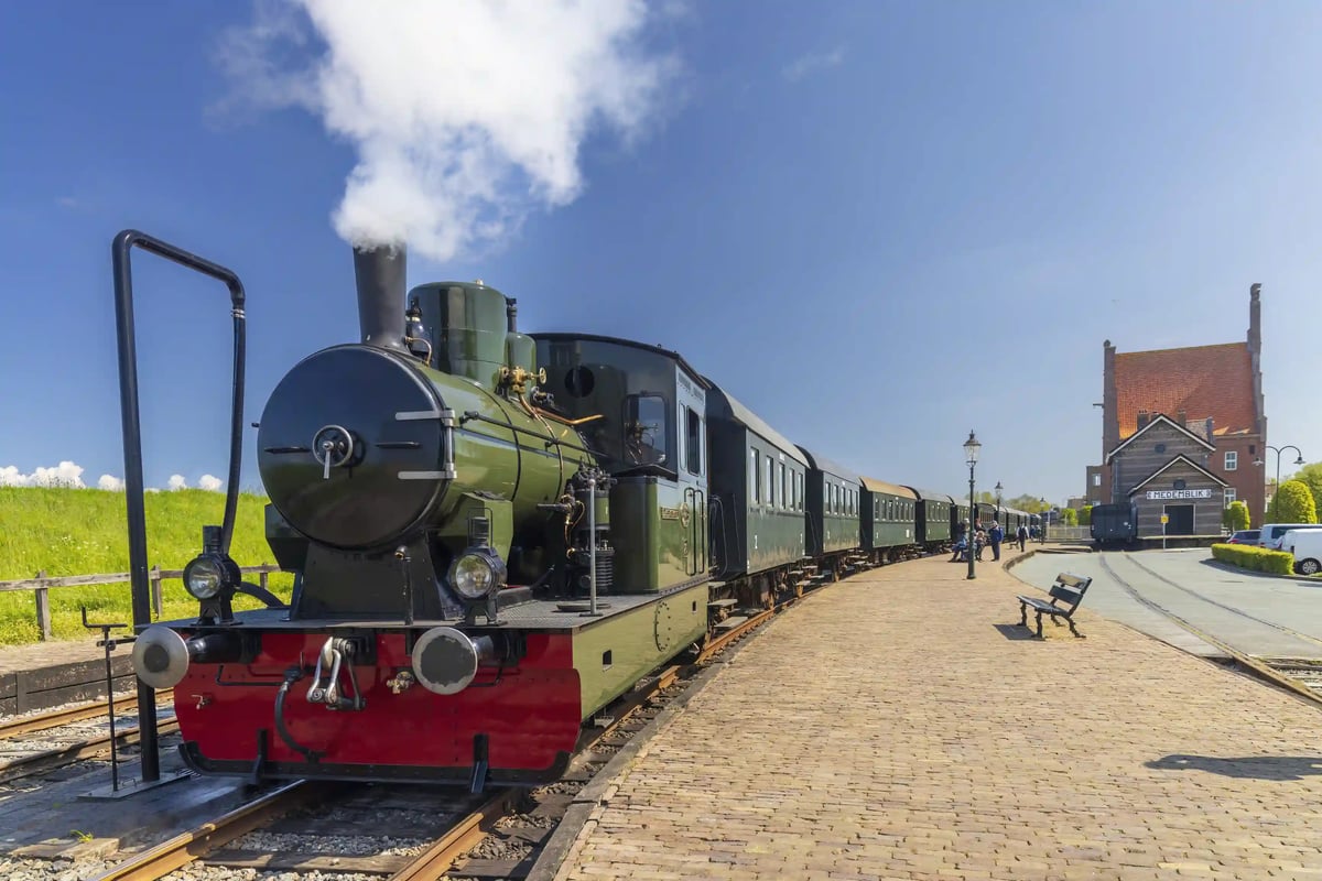 Grüne historische Dampflok mit Waggons steht am Bahnsteig bei sonnigem Wetter