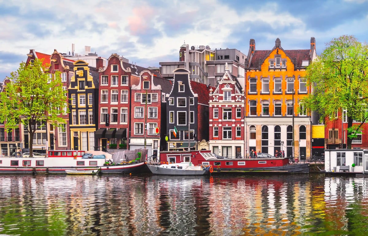 Typische Grachtenhäuser mit Bäumen und Booten entlang eines Kanals in Amsterdam