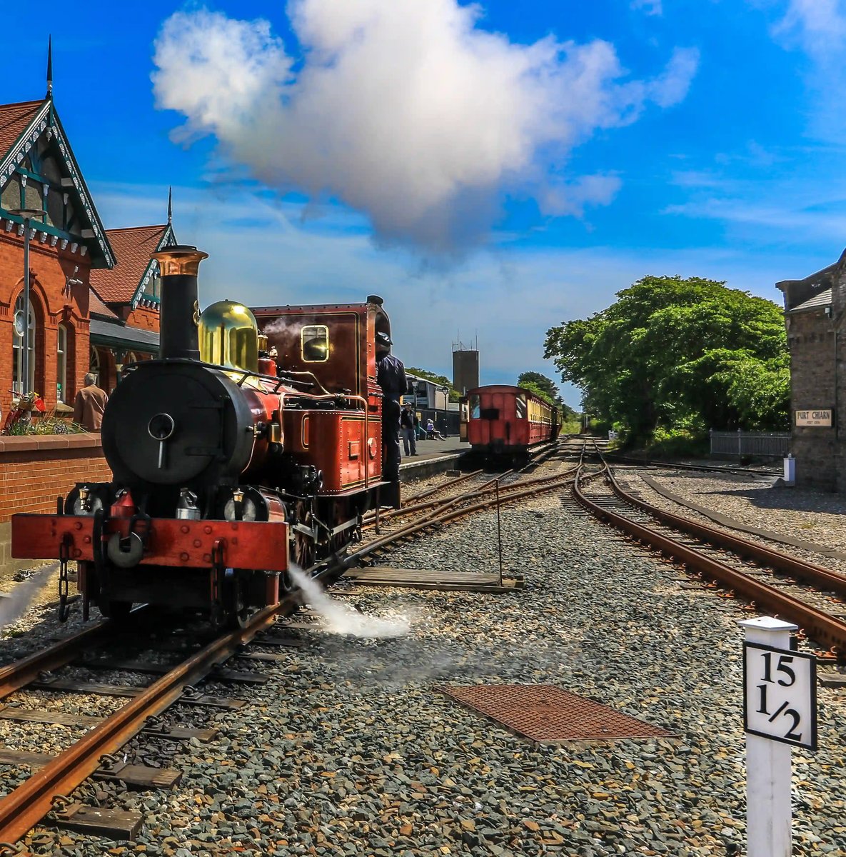 Rote Dampflokomotive am Bahnhof, Dampf steigt auf, Gleise führen in die Ferne unter blauem Himmel