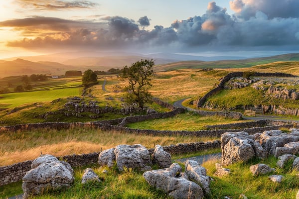 Hügellandschaft mit Steinmauern und Wiesen im Abendlicht, dramatische Wolken über weitem Tal