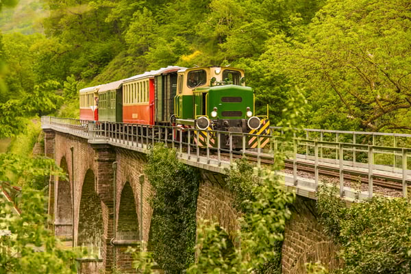 Historischer Vulkan Express fährt über ein Steinviadukt durch grüne Landschaft der Eifel