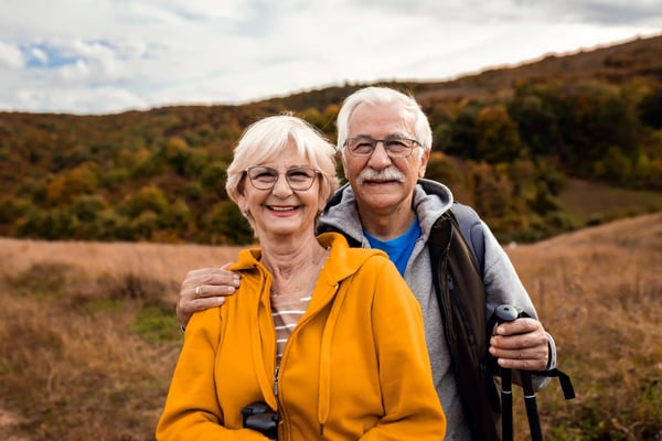 Älteres Paar mit Wanderstöcken lächelt in herbstlicher Landschaft der Eifel bei einer gemeinsamen Wanderung