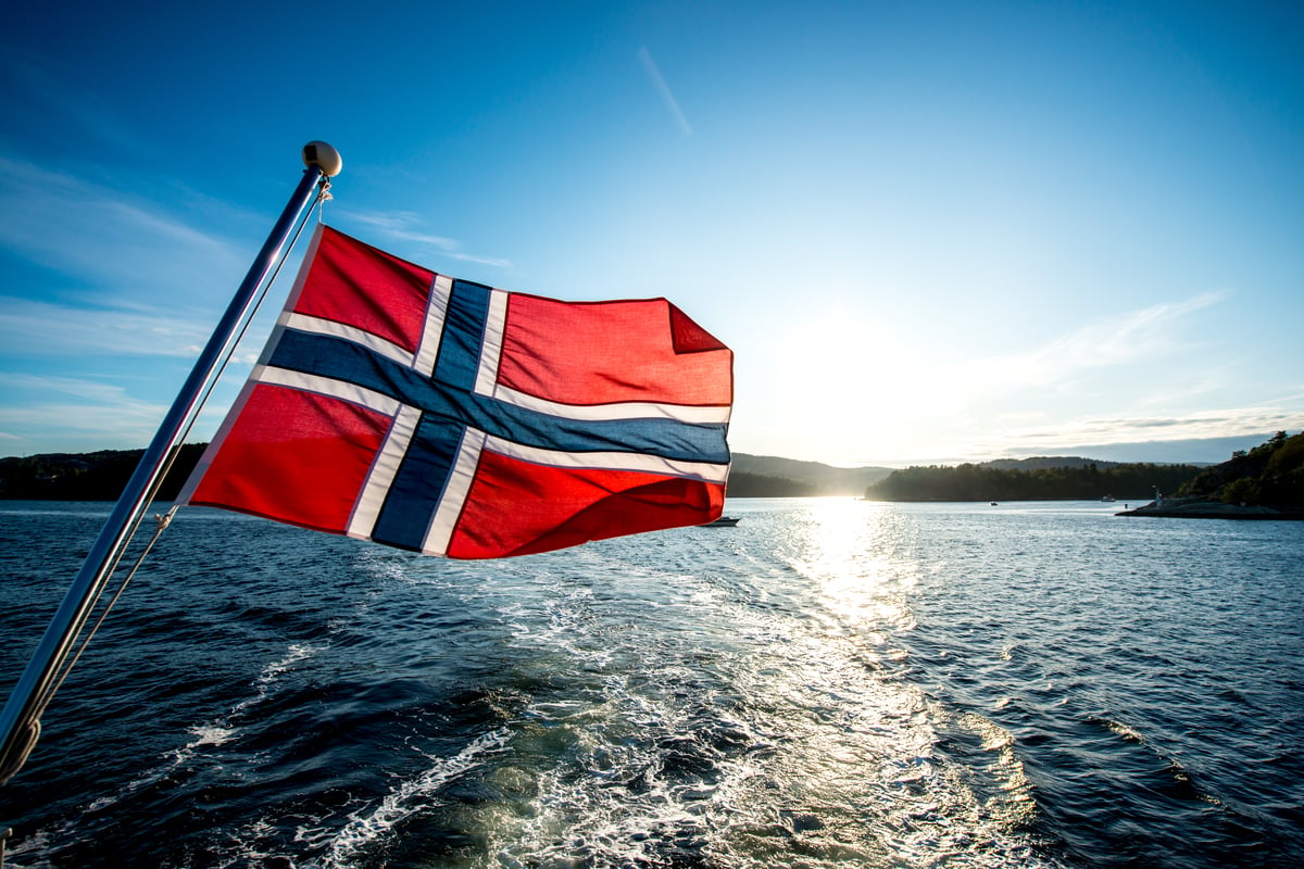 Norwegische Flagge am Heck eines Schiffes mit Blick auf die Küstenlandschaft
