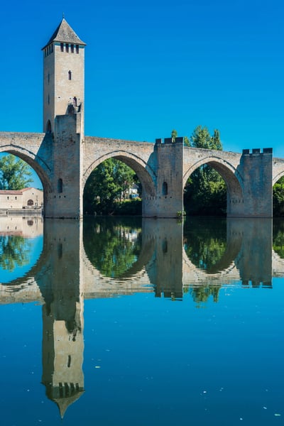 Historische Steinbrucke mit hohem Turm spannt sich uber ruhigen Fluss, Spiegelbild im Wasser