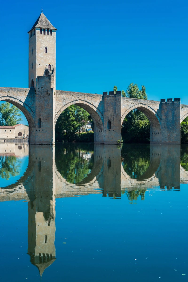 Pont en pierre historique avec haute tour au-dessus d'une riviere calme, reflet net dans l'eau