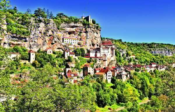 Mittelalterliche Hauser und Kirchen kleben an einer steilen Felswand uber grünem Tal unter blauem Himmel