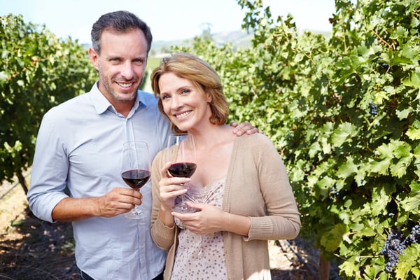 Paar im Weinberg halt Rotweinglaser und lachelt zwischen Reben mit Trauben