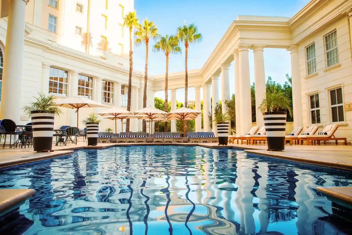 Heller Innenhof mit Pool, weissen Säulen, Sonnenschirmen und Palmen vor einem eleganten Gebäude